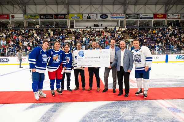 Players and sponsors on the ice presenting large donation cheque