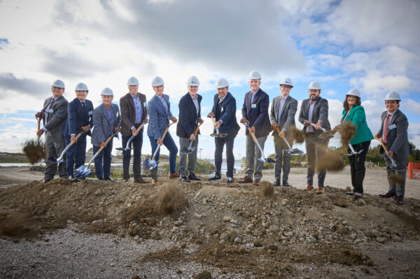 Company partners wearing hard hats and holding shovels for the first ground breaking of construction site